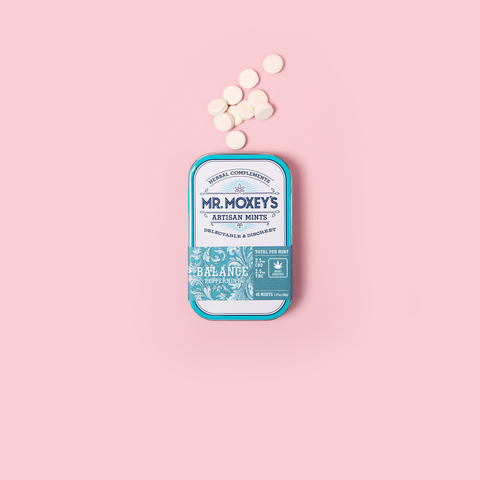 A tin of Mr. Moxey's THC and CBD Balance mints with loose mints on a pink background